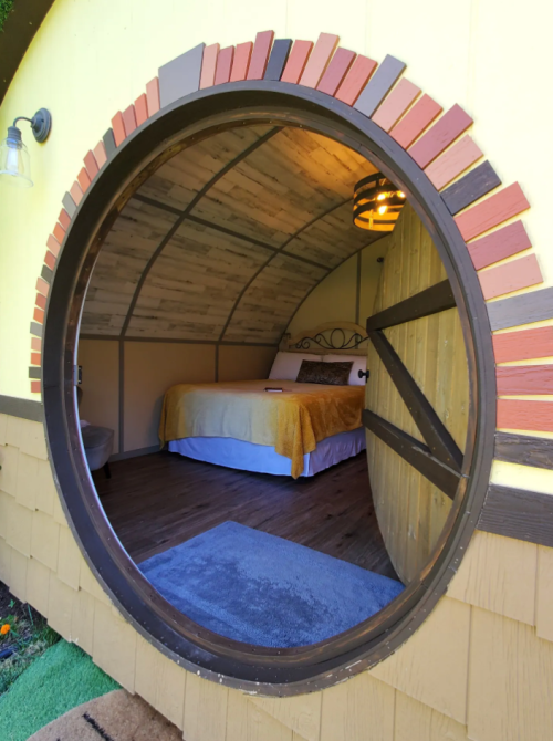 A cozy round entrance leads to a charming bedroom with a bed and warm decor inside a yellow structure.